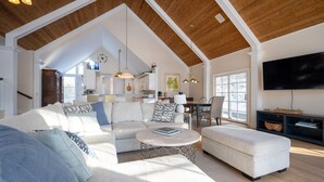 A spacious living room with a high ceiling, a large sofa, a coffee table, and a television. - Beautiful Lake Michigan Home Great for Large (West Olive)