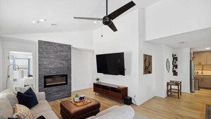 Un saló modern amb una llar de foc, un televisor de pantalla plana fixat a la paret i un ventilador de sostre.