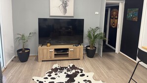 Una sala de estar con un televisor de pantalla plana sobre un soporte de madera, dos plantas en macetas, un tapiz de cuero de vaca y una pintura de Buda en la pared.