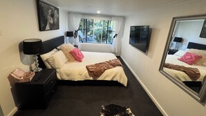 Una habitación de hotel con cama, mesita de noche, lámpara, espejo y ventana con cortinas.