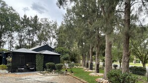 Un espacio de estar al aire libre cubierto, con una mesa y sillas, rodeado por un jardín con árboles y césped.