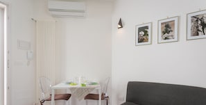 Ein modernes Wohnzimmer mit einem grauen Sofa, einem Esstisch mit Stühlen und drei gerahmten Bildern an der Wand.