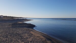 A beach with a rocky shoreline, a calm sea, and buildings in the background. - Charming penthouse with an ocean view a few steps from the train and bus station (Lido di Ostia)