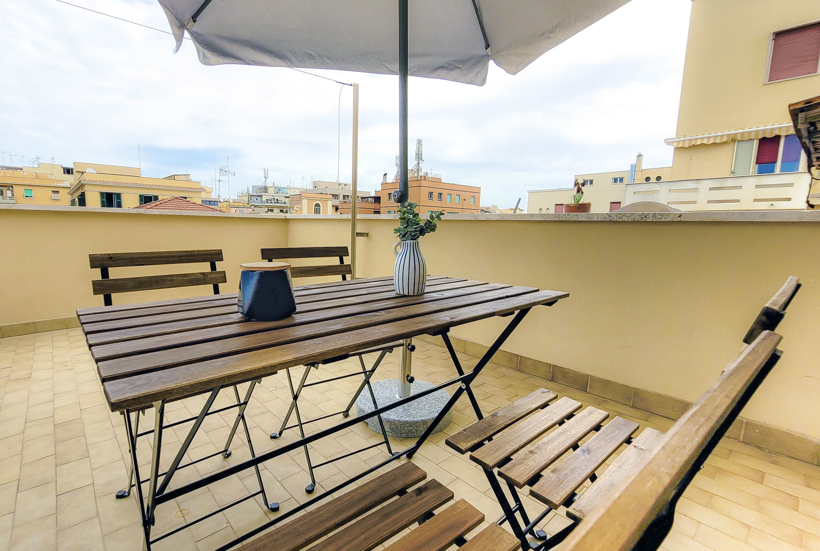 A wooden table with benches, a potted plant, and an umbrella on a rooftop terrace.