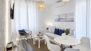 A modern living room with a white sofa, blue cushions, a round white table, and a wicker pendant light. - Charming penthouse with an ocean view a few steps from the train and bus station (Lido di Ostia)