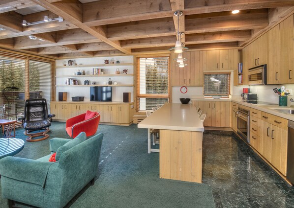 Una cocina moderna con armarios de madera, una isla central y una zona de comedor con un sofá verde y una silla roja.