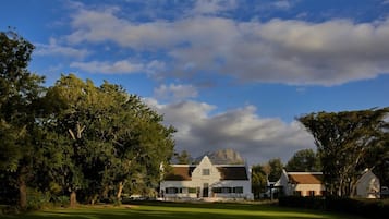 Un bâtiment blanc à la façade symétrique, entouré d’une végétation luxuriante et sous un ciel dégagé.