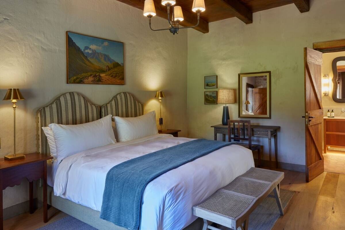 Een slaapkamer met een groot bed, bedlampjes, een bureau en een badkamer zichtbaar door een geopende deur.