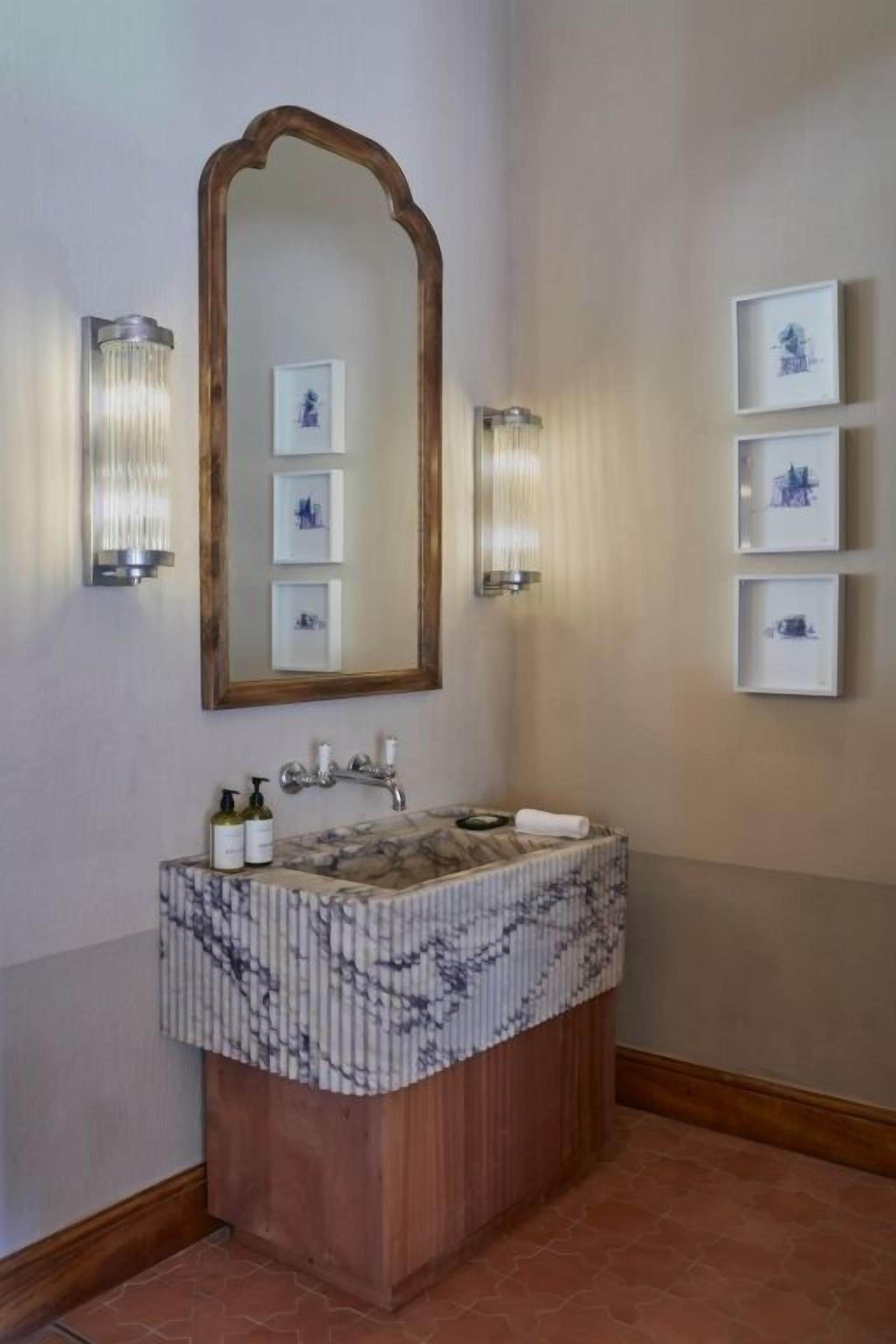 Une salle de bain avec un lavabo en marbre, un meuble-lavabo en bois et des tableaux encadrés accrochés au mur.