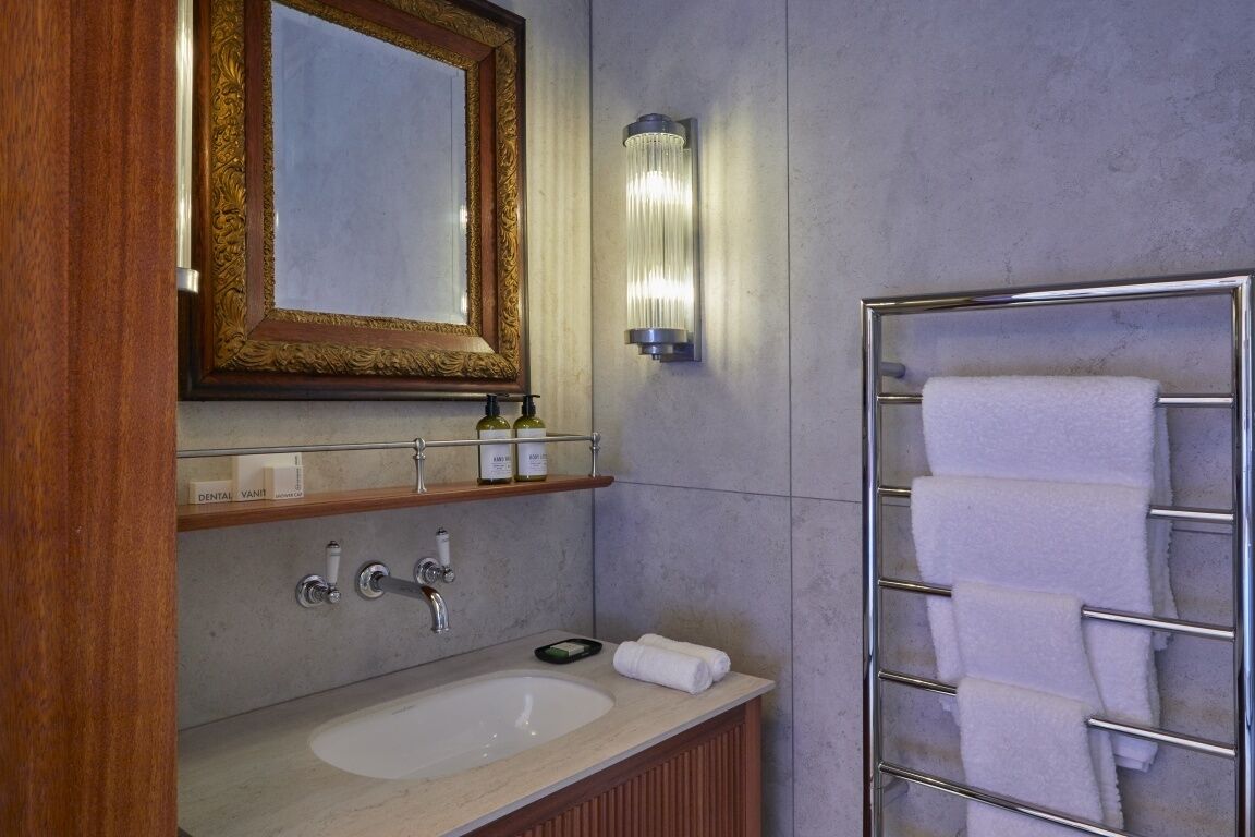 Een badkamer met een wastafel, spiegel, handdoekhouder en een wandlamp.
