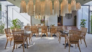 Un área de comedor al aire libre con sillas de mimbre y una mesa lista para una comida, con lámparas colgantes.