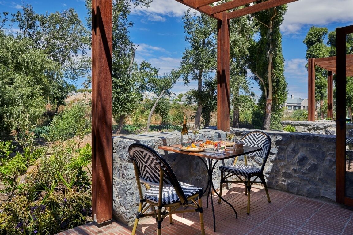 An outdoor patio with a stone wall, wooden pergola, and two chairs.