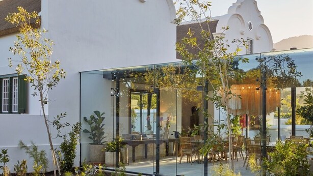 Una casa moderna con un invernadero de vidrio, mobiliario exterior y fachada blanca.