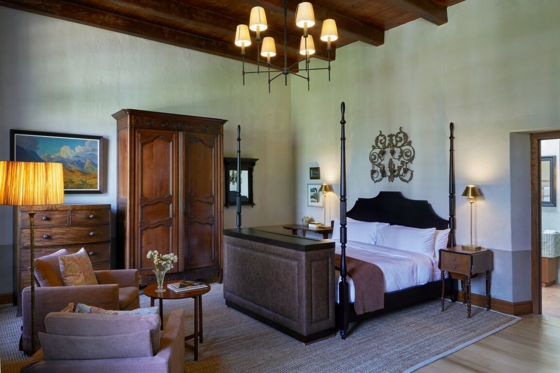 A bedroom with a large bed, a wooden dresser, a desk, a chair, and a painting on the wall.