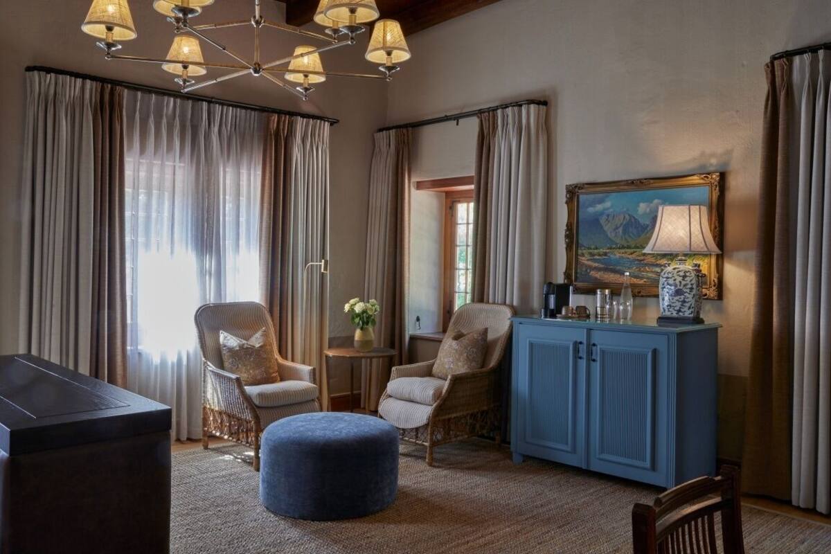 Een gezellige kamer met een blauwe kast, rieten stoelen, een rond poef en een kroonluchter.