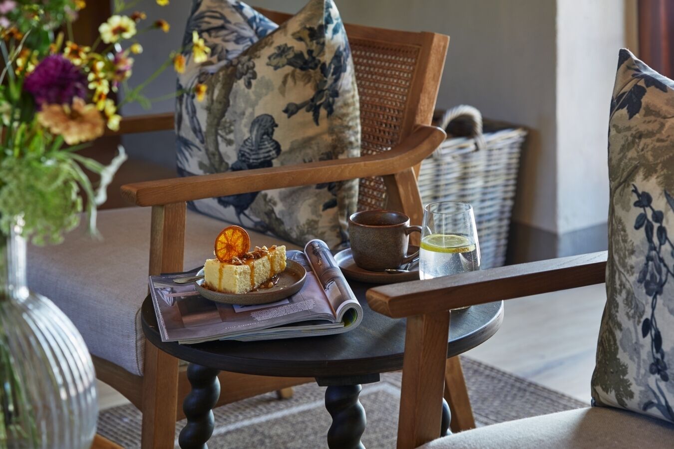A wooden chair with a cushion, a small table with a dessert, a cup, and a glass of water.