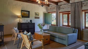 A cozy living room with a sofa, chairs, a coffee table, and a cabinet. There is a painting on the wall and a window with curtains.