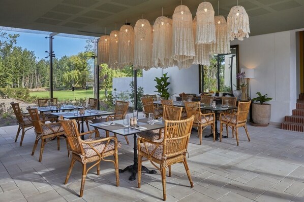 Un espace de restauration en plein air, aménagé avec des meubles en osier et des luminaires suspendus.