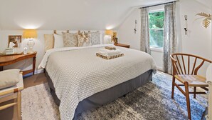 Une chambre à coucher avec un grand lit, une chaise en bois, une table de chevet, une lampe et une fenêtre avec des rideaux.