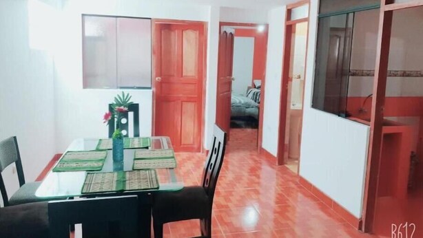 A dining area with a glass table, chairs, and a red door leading to a bedroom. - Umary Wai ............................. (Cusco)