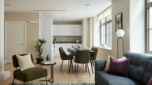 Un salon moderne avec un canapé gris, un fauteuil vert et un coin repas comprenant une table et des chaises.