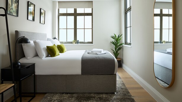 Une chambre à coucher moderne avec un grand lit, une table de chevet, un miroir et une fenêtre.