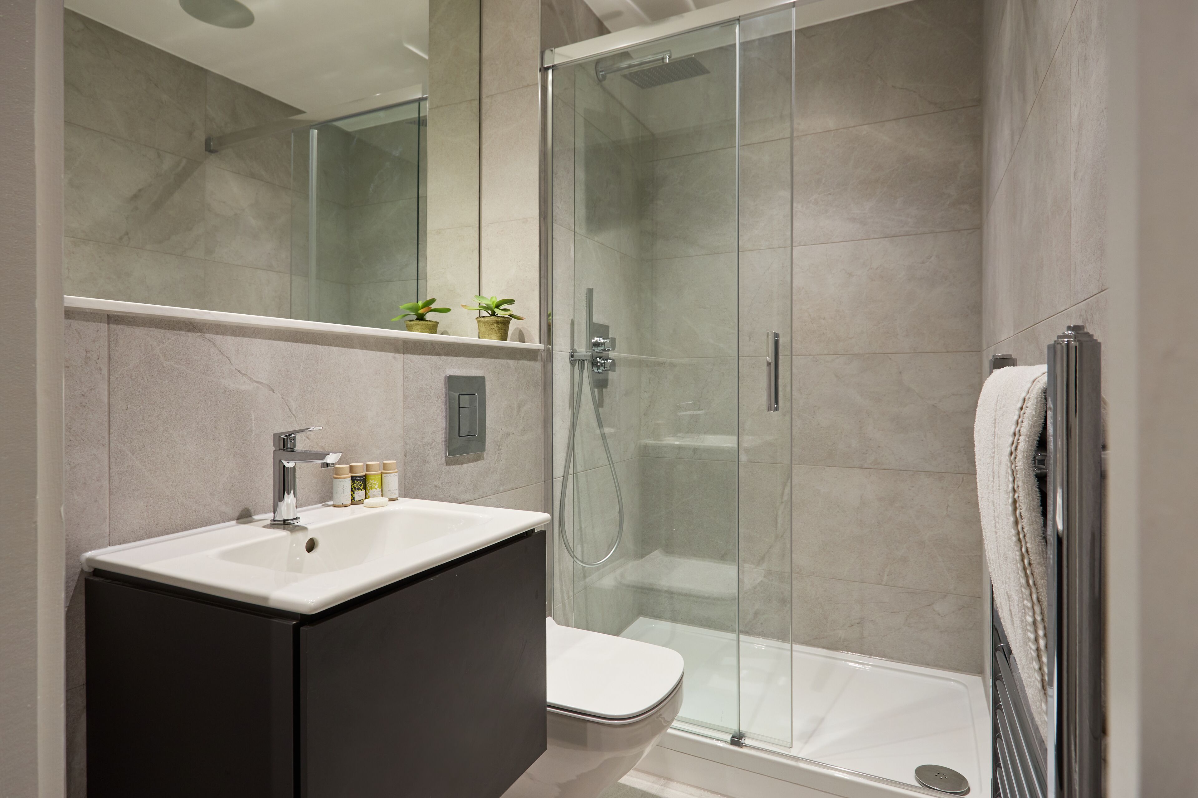 Un baño moderno con ducha envuelta en vidrio, un lavamanos blanco y un mueble de tocador en tonos oscuros.