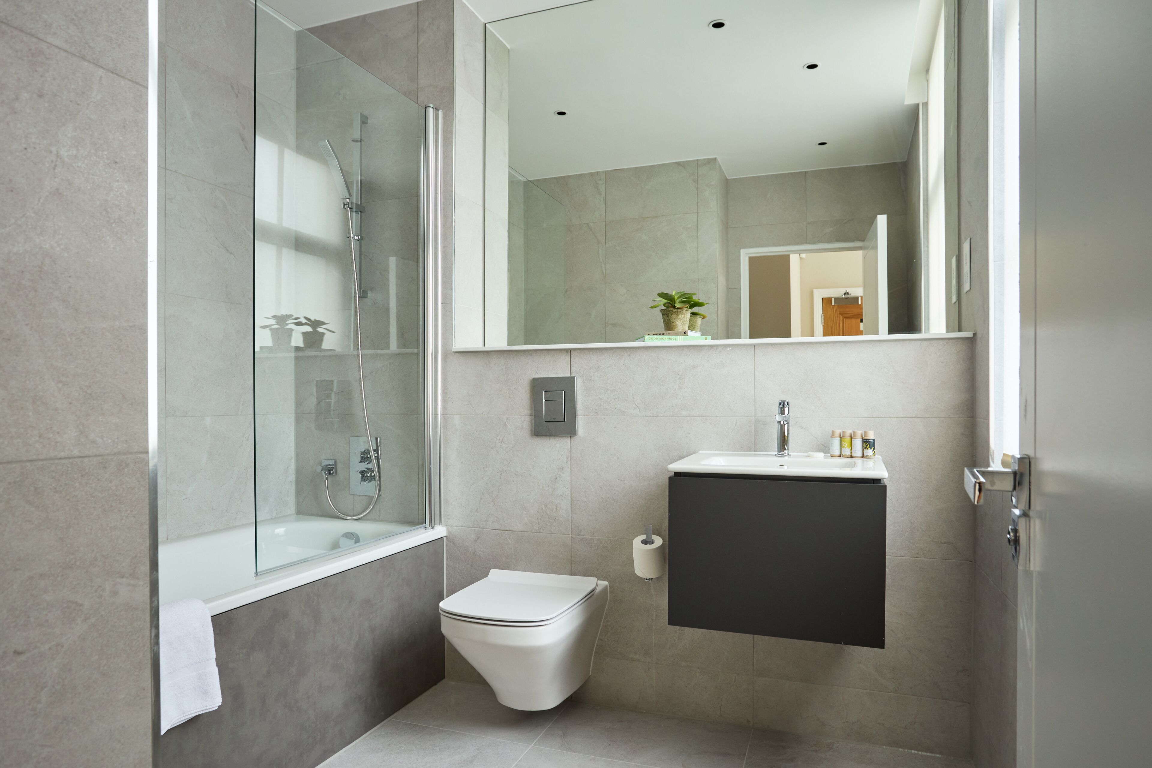 Une salle de bain moderne avec une douche à parois de verre, des toilettes blanches, un lavabo avec un meuble sombre en dessous et un miroir au-dessus du lavabo.