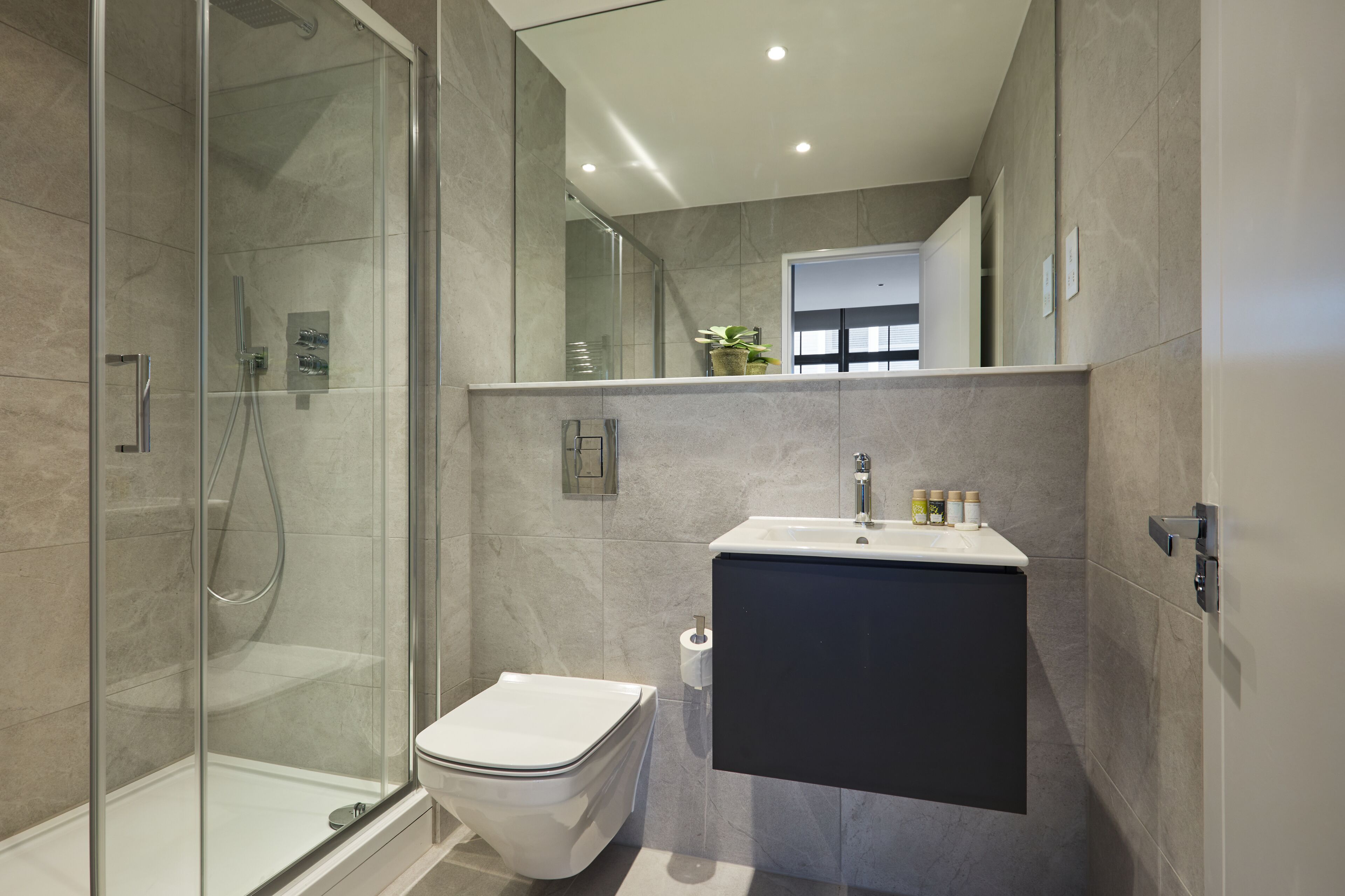 Un baño moderno con ducha de vidrio, inodoro blanco y tocador oscuro con lavamanos.