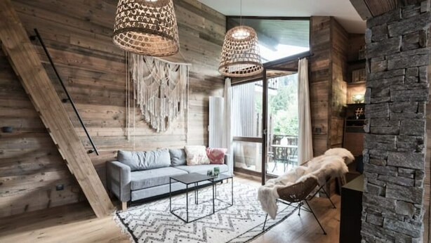 Un salon moderne avec un plafond en pente en bois, un canapé gris, une table basse et une cheminée en pierre.