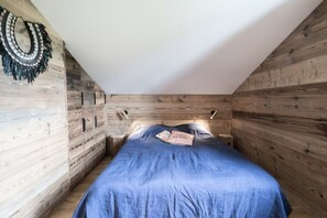 A bedroom with a wooden slat wall, a blue bedspread, and a decorative wall hanging. - Bel Appartement Neuf 3 Chambres (Megève)