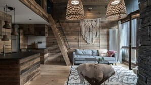 Un intérieur moderne avec des poutres apparentes, un coin cuisine, un canapé avec des coussins et deux lampes suspendues en osier.