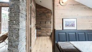 Un couloir étroit, avec un mur de pierre d’un côté et un mur en bois de l’autre. Au bout du couloir, on trouve un banc muni d’un coussin.