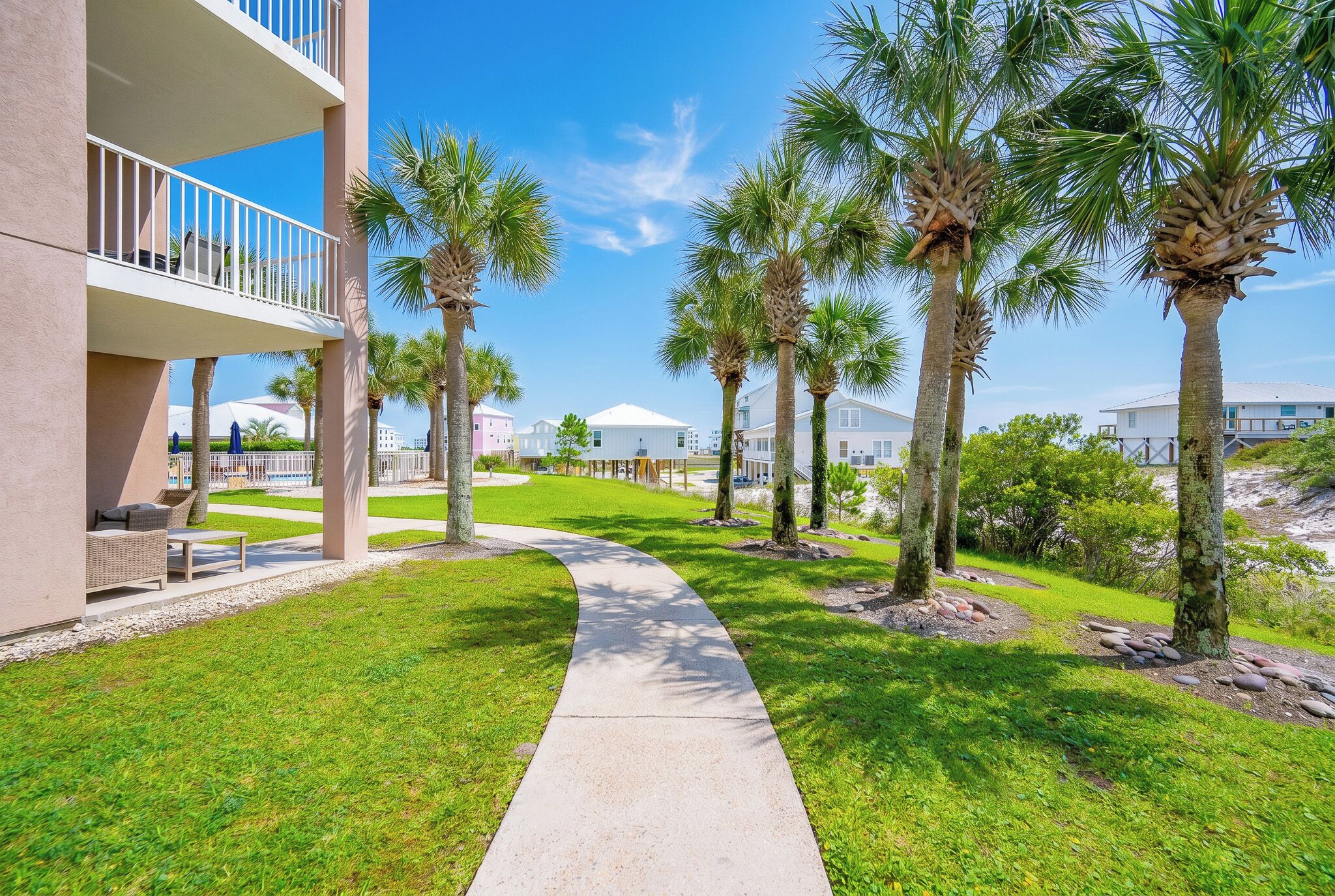 A pathway lined with palm trees, a building with balconies, and a clear sky.