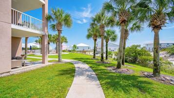 A pathway lined with palm trees, a building with balconies, and a clear sky.