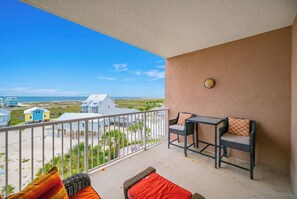 Un balcon avec vue sur la plage, une table avec des chaises et un petit tapis.