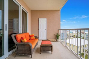 A balcony with a wicker sofa and ottoman, a sliding glass door, and a view of neighboring buildings.