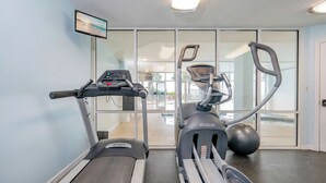 Un gimnasio con cintas de correr y una máquina elíptica, un televisor en la pared y vistas a través de puertas de cristal.
