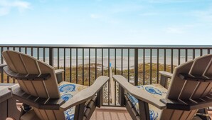 A balcony with two Adirondack chairs facing a beach.