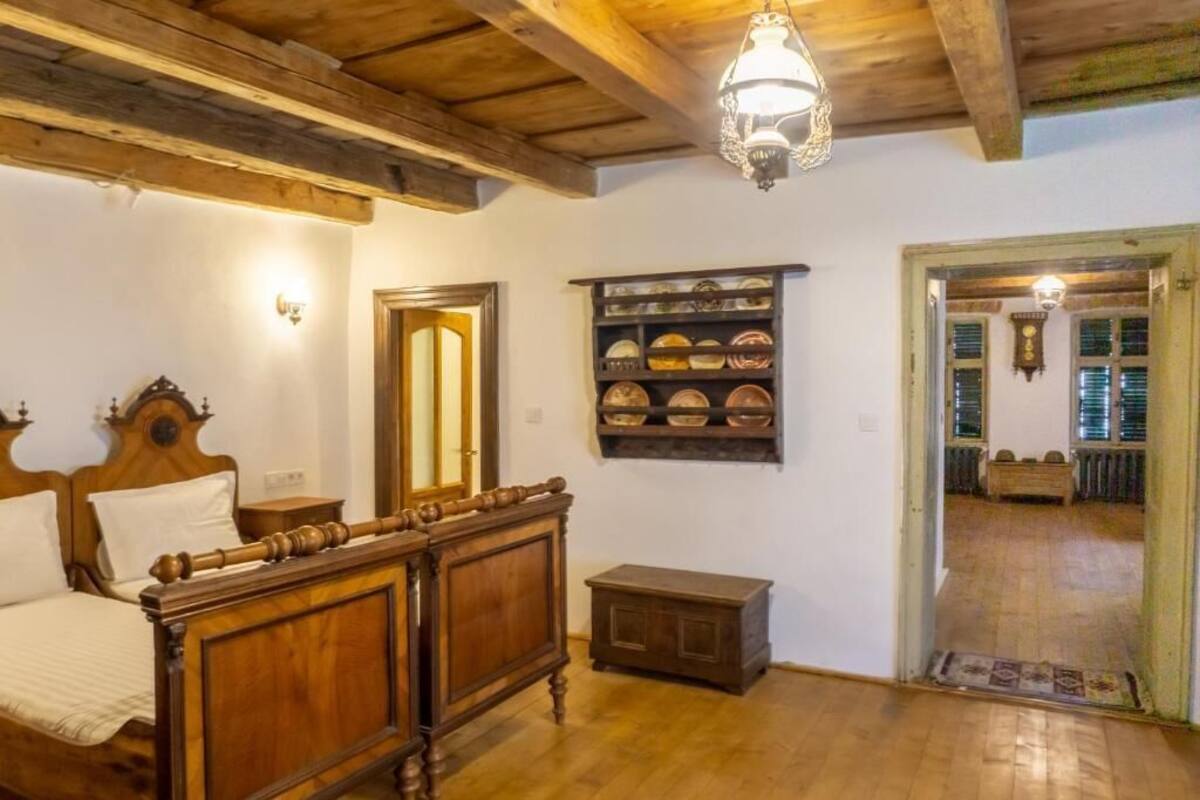 Una cama con estructura de madera, una mesita de noche, un estante con vajilla y un armario de madera.