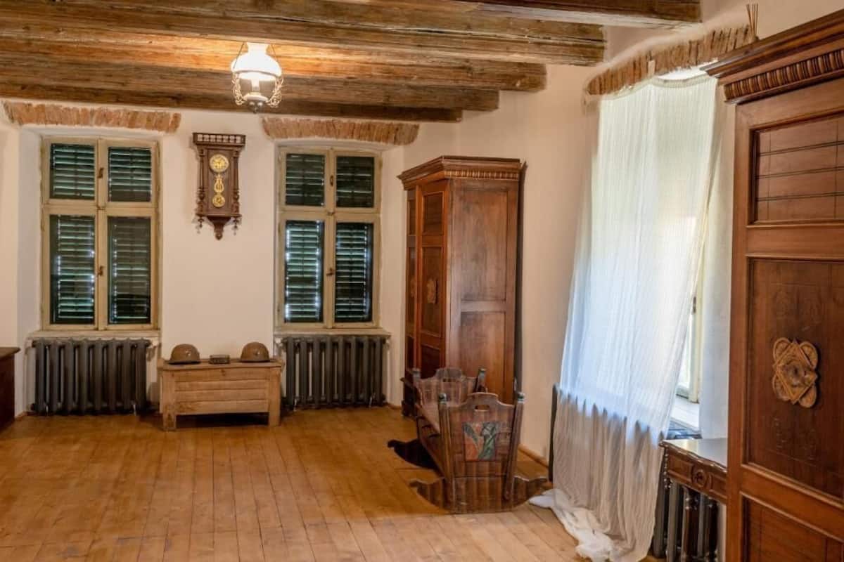 Una habitación con pisos de madera, un radiador, un banco de madera, un armario de madera y una puerta grande de madera.