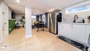 A modern kitchen with white cabinets, a stainless steel refrigerator, and a dining area with a table and chairs.