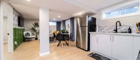 Una cocina moderna con armarios blancos, un refrigerador de acero inoxidable y una zona de comedor con mesa y sillas.