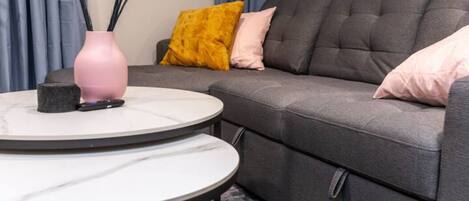 Un salon avec un canapé gris, deux tables rondes et des coussins décoratifs.