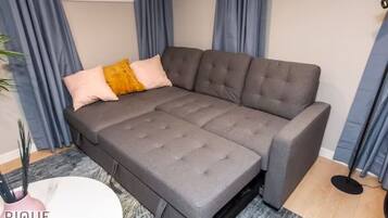 A grey sectional sofa with a grey and yellow accent pillow, a white side table, and a grey rug.