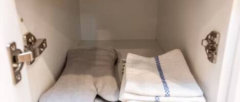 A white cabinet with a grey cushion and folded towels.