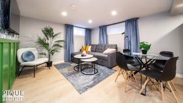 A modern living room with a sofa, two side tables, a coffee table, and a dining area with chairs and a table.