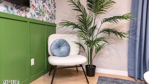 A room with a green wall, a white chair with a blue cushion, and a tall potted plant.