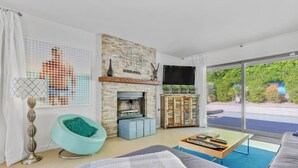 A modern living room with a stone fireplace, a television, and a view of greenery outside.