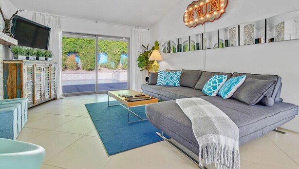 A modern living room with a grey sofa, blue and white patterned cushions, a coffee table, and a TV on a wooden cabinet.